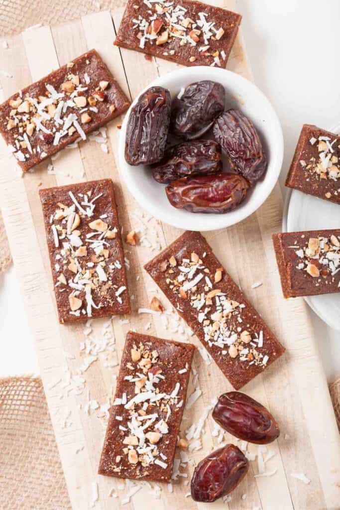 6 Date Bars topped with coconut and nuts around a bowl of dates. 