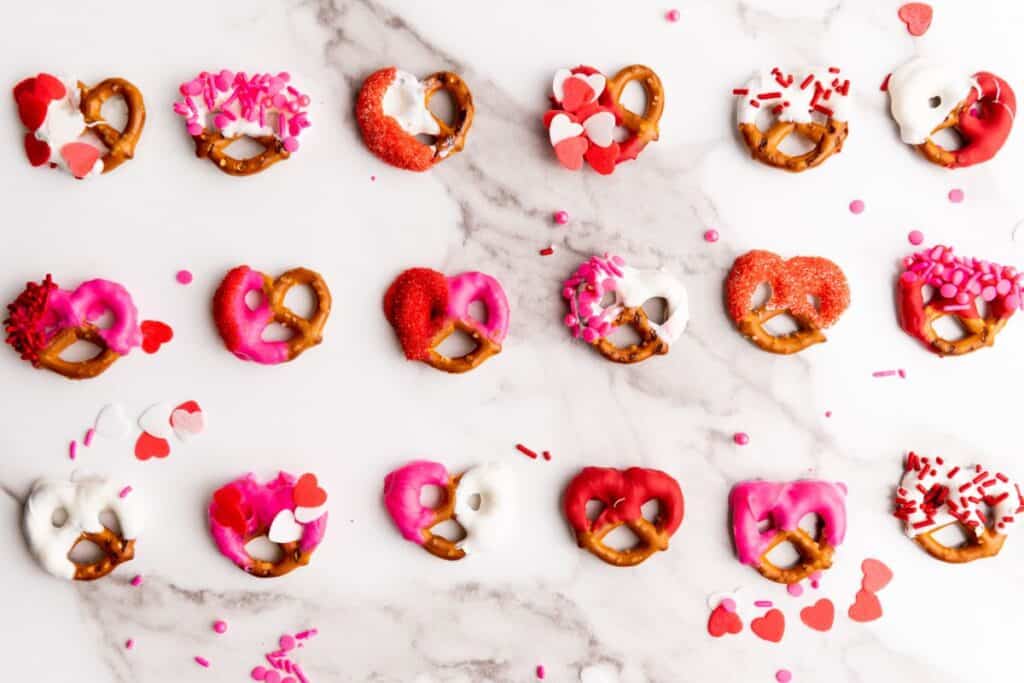 Three rows of Valentine's themed mini pretzels half dipped in red, white or pink candy melts, and decorated with sprinkles. 