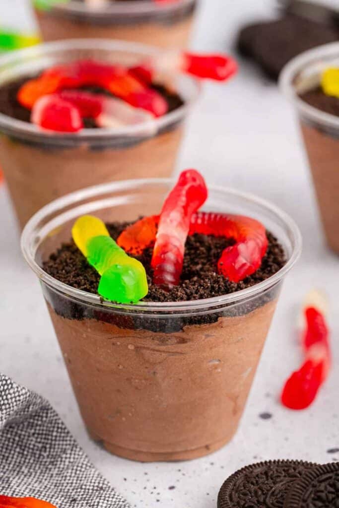 Dirt and Worms Cups filled with creamy chocolate pudding and topped with crushed chocolate cookies to resemble soil. Bright red and green gummy worms crawl across the cookie crumbs for a playful dessert.