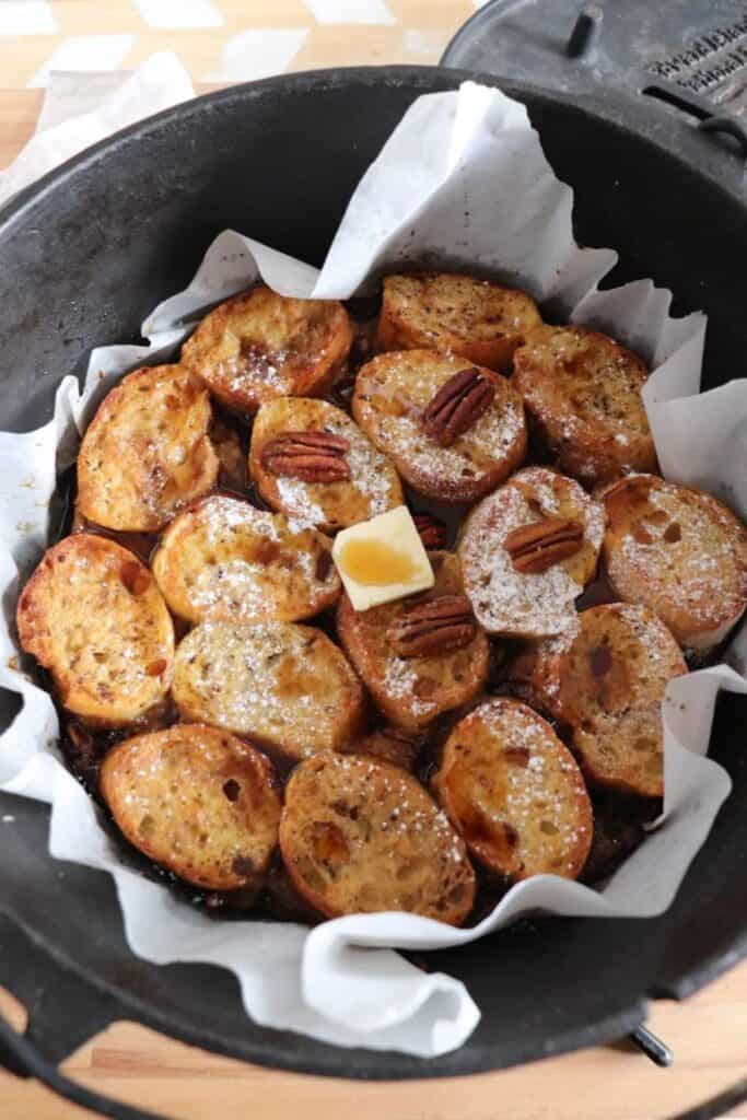 Cast iron dutch oven filled with small rounds of french toast with pecans and butter on top.