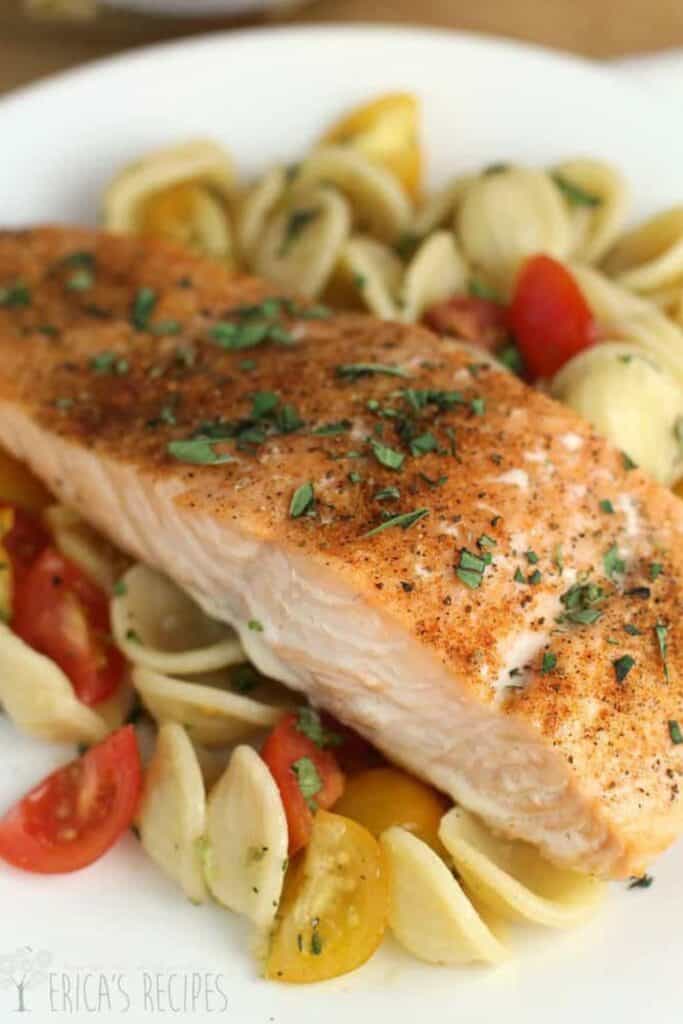 Piece of baked salmon over pasta with herbs and cherry tomatoes. 