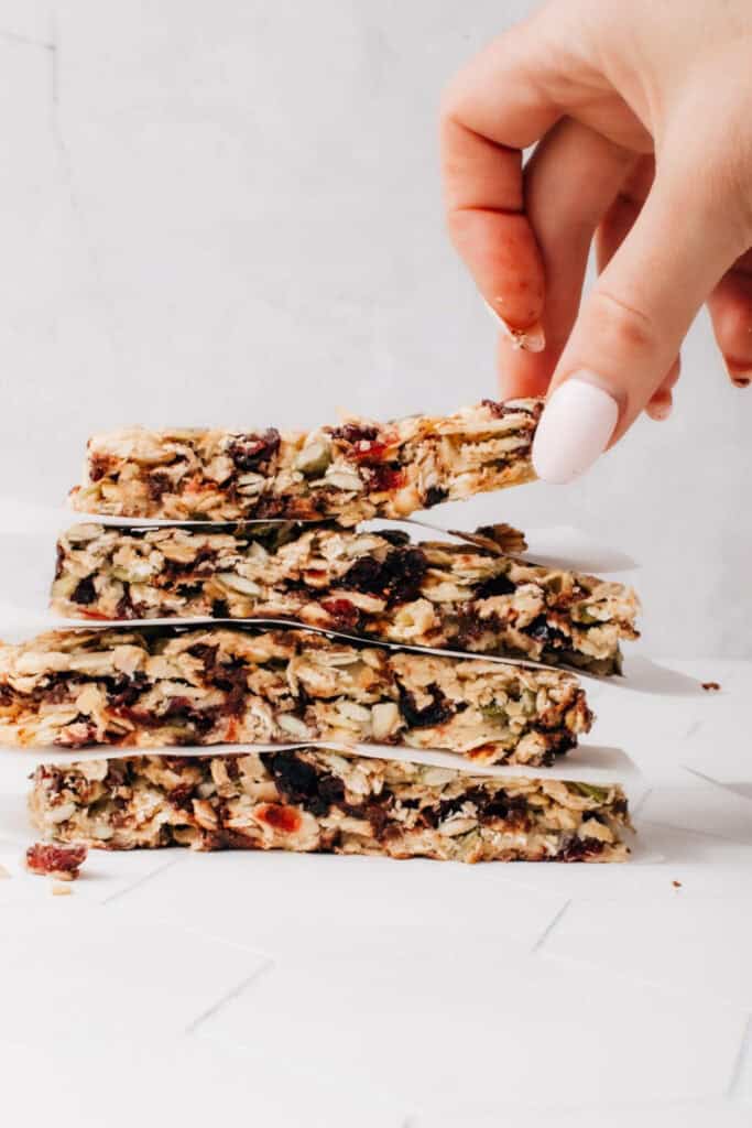 A stack of four homemade healthy granola bars with dired fruit, with a hand grabbing the top one. 