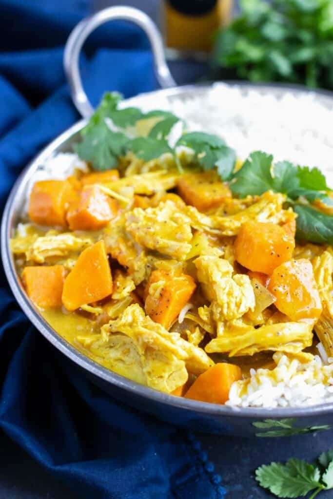 Close up of a metal bowl filled with Chicken curry with sweet potatoes , and white rice. 