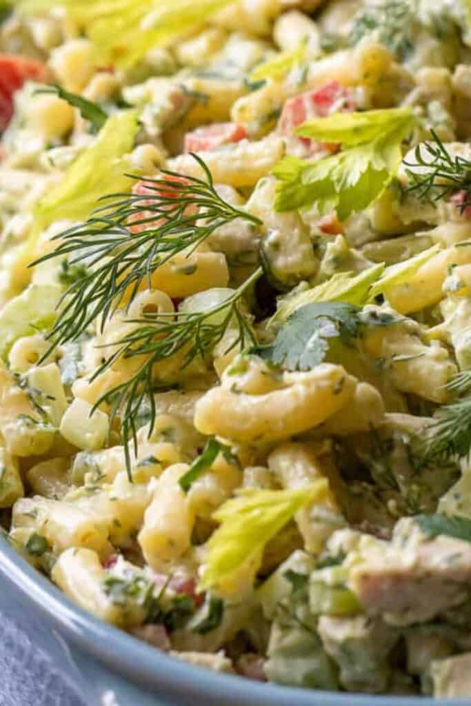 Close up of a bowl of creamy chicken macaroni pasta salad topped with fresh dill. 