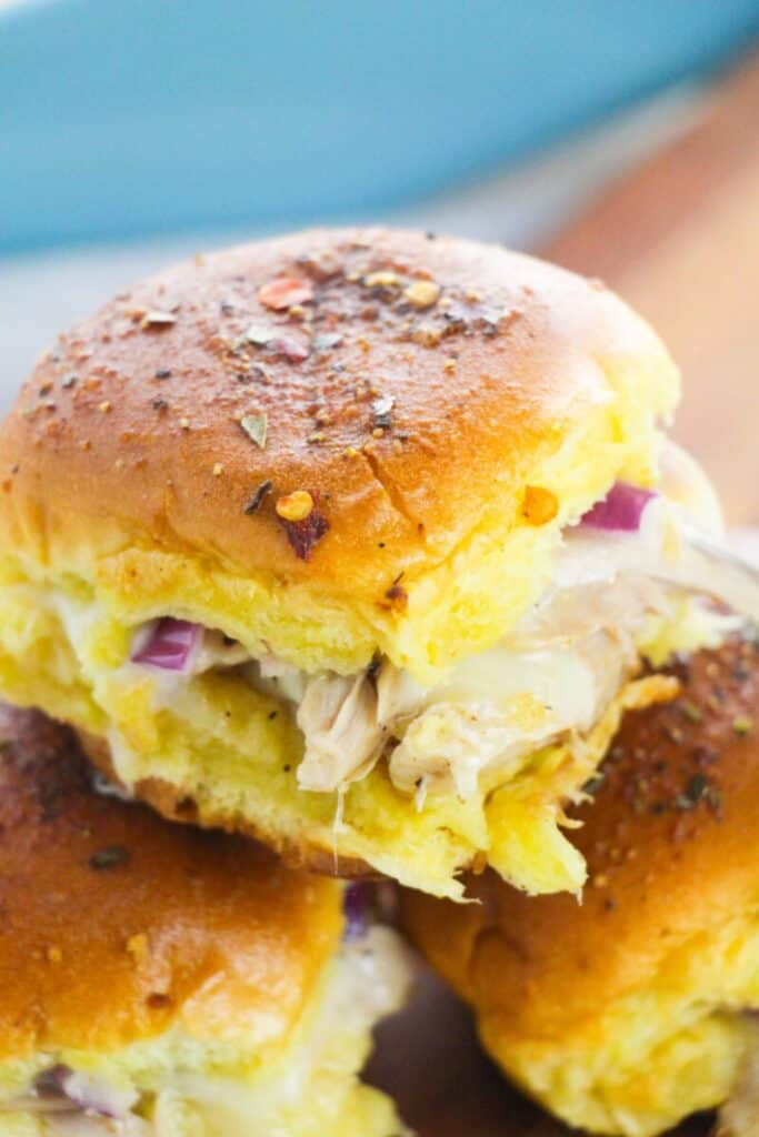 Easy chicken sliders made with soft golden rolls filled with shredded chicken, melted cheese, and diced red onion. Close up of the warm baked sliders with seasoned tops showing the cheesy chicken filling for a simple weeknight dinner.