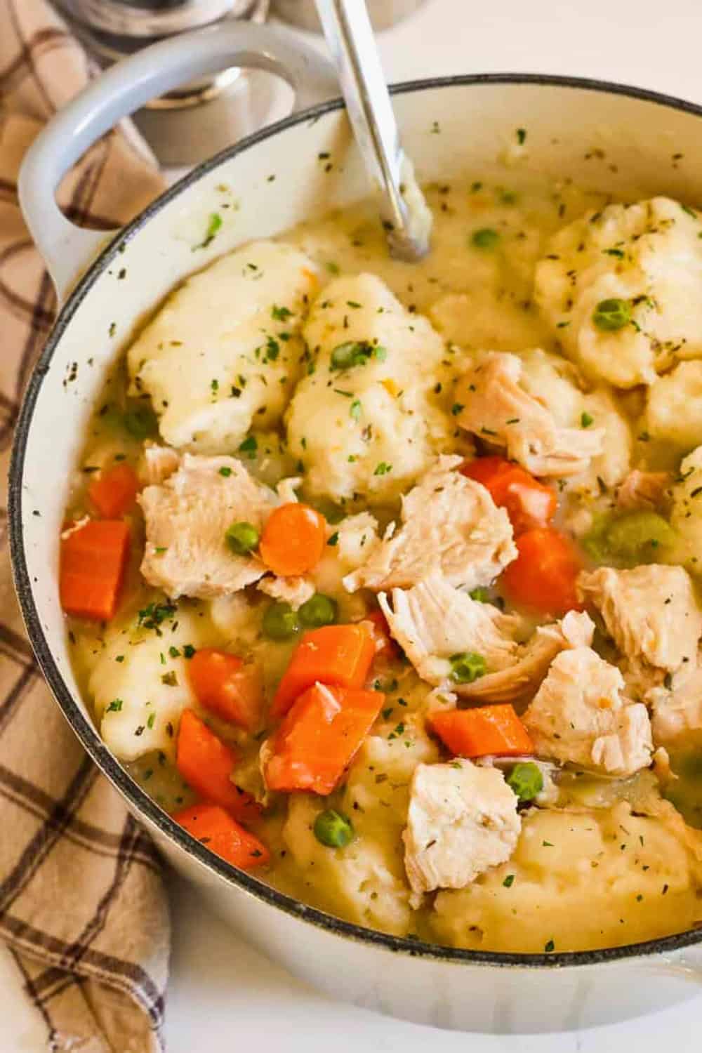 Easy chicken and dumplings with tender chicken carrots peas and fluffy dumplings are served in a thick savory broth. The hearty dish fills a large pot ready for serving.
