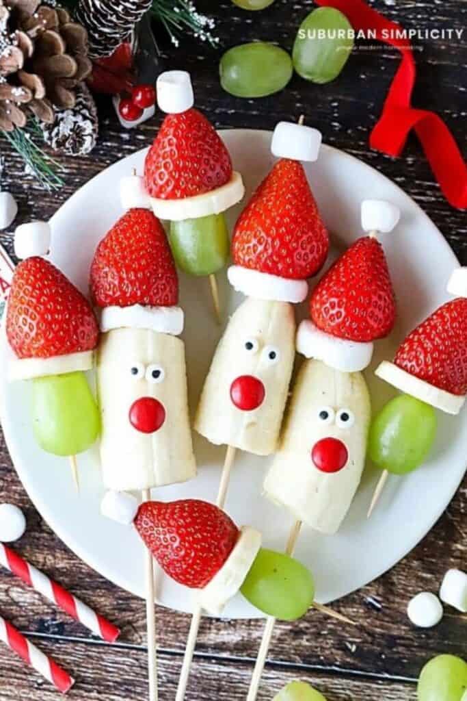 Plate of santa and grinch fruit kabobs made out of green grpas, strawberries and mini marshmallows. 