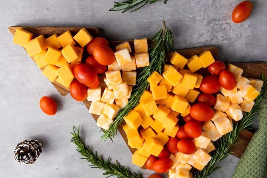 Christmas tree wooden platter with alternating layers of cheese cubes, cherry tomatoes and rosemary sprigs.