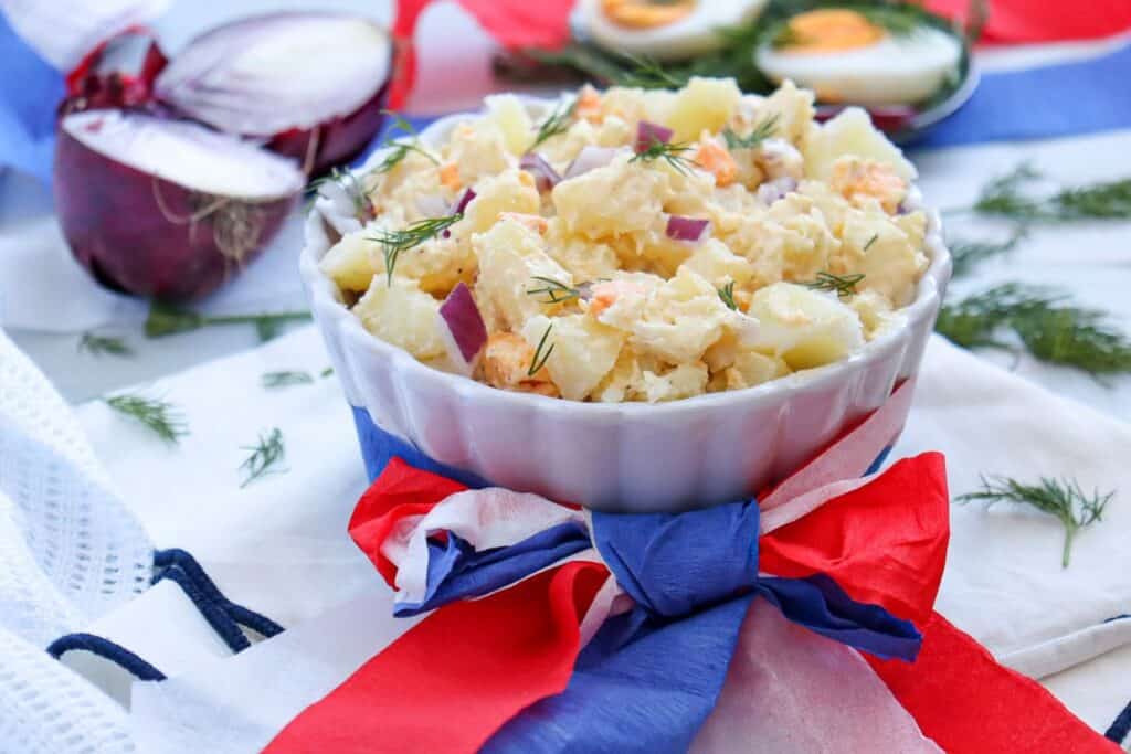 Medium sized scalloped dish filled with potato salad, and wrapped in a red white and blue bow. 