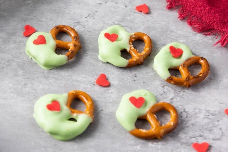 5 Christmas Pretzels inspired by the Grinch, half dipped in green chocolate with a tiny candy heart.