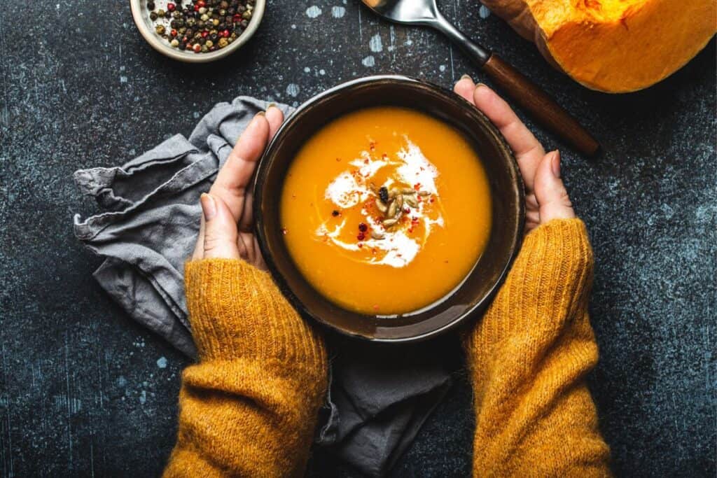 Hands holding a bowl of fall pumpkin soup.