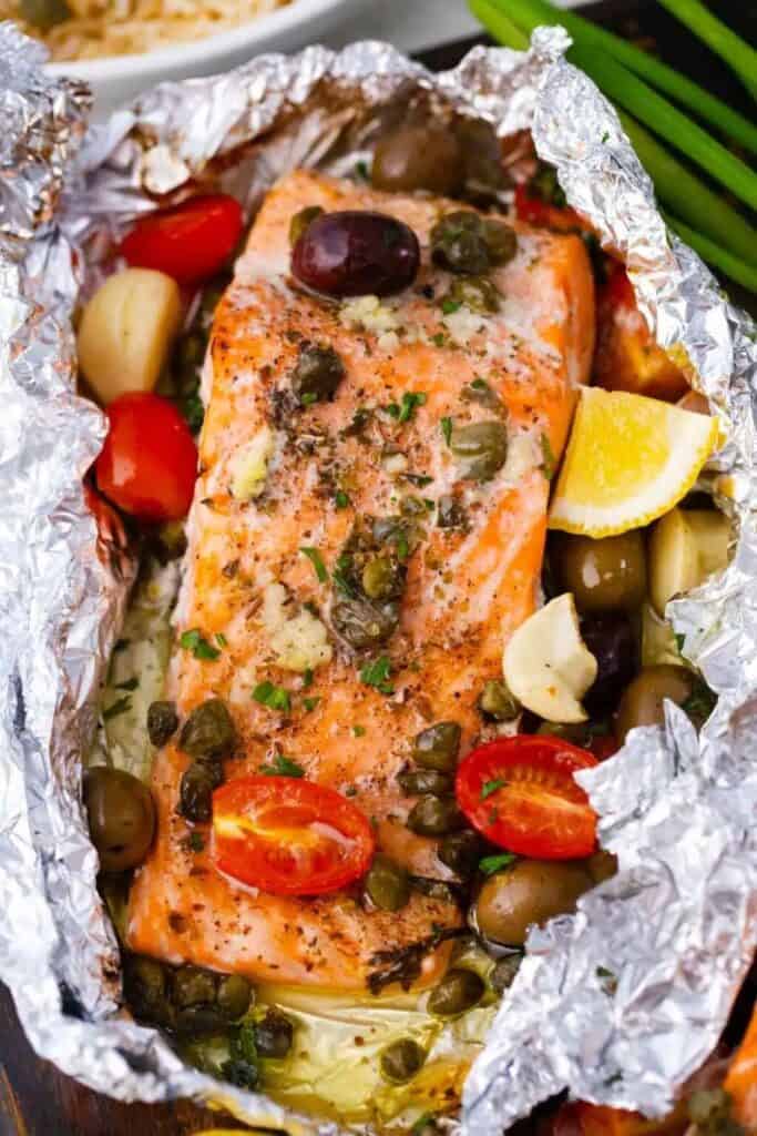 Open Mediterannean foil packet with baked salmon topped with cherry tomatoes, lemon slices and olives. 