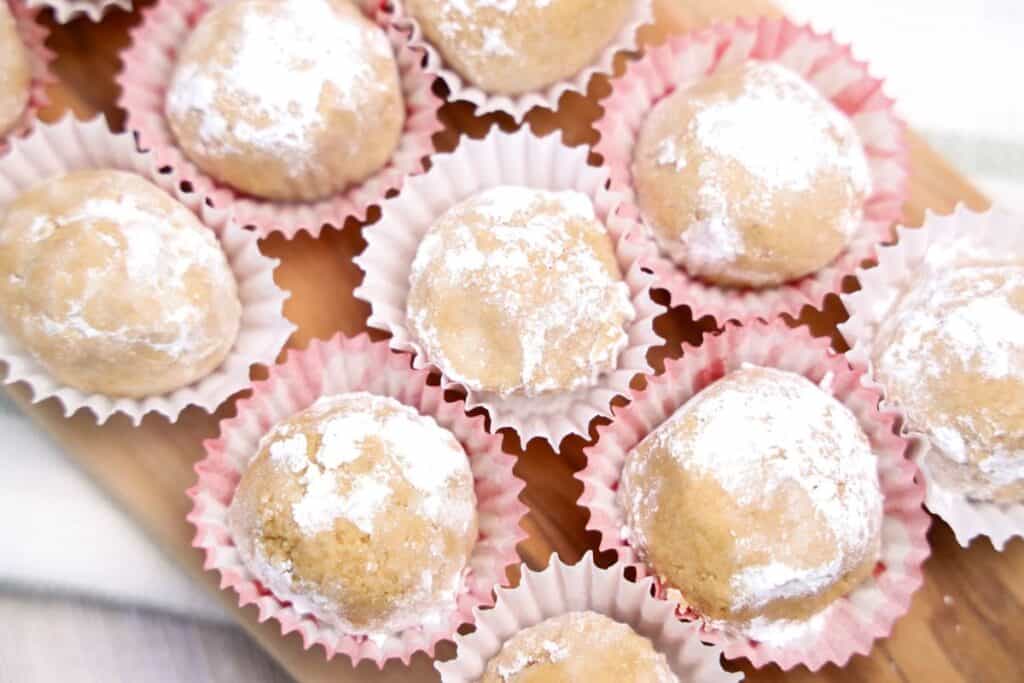 Nine small no bake peanut putter balls rolled in icing sugar in mini cupcake liners on a wooden board.