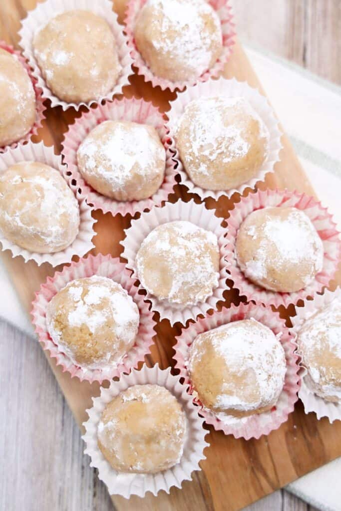 Close up of 12 peanut butter snowball treats in mini cupcake wrappers on a wooden board. 