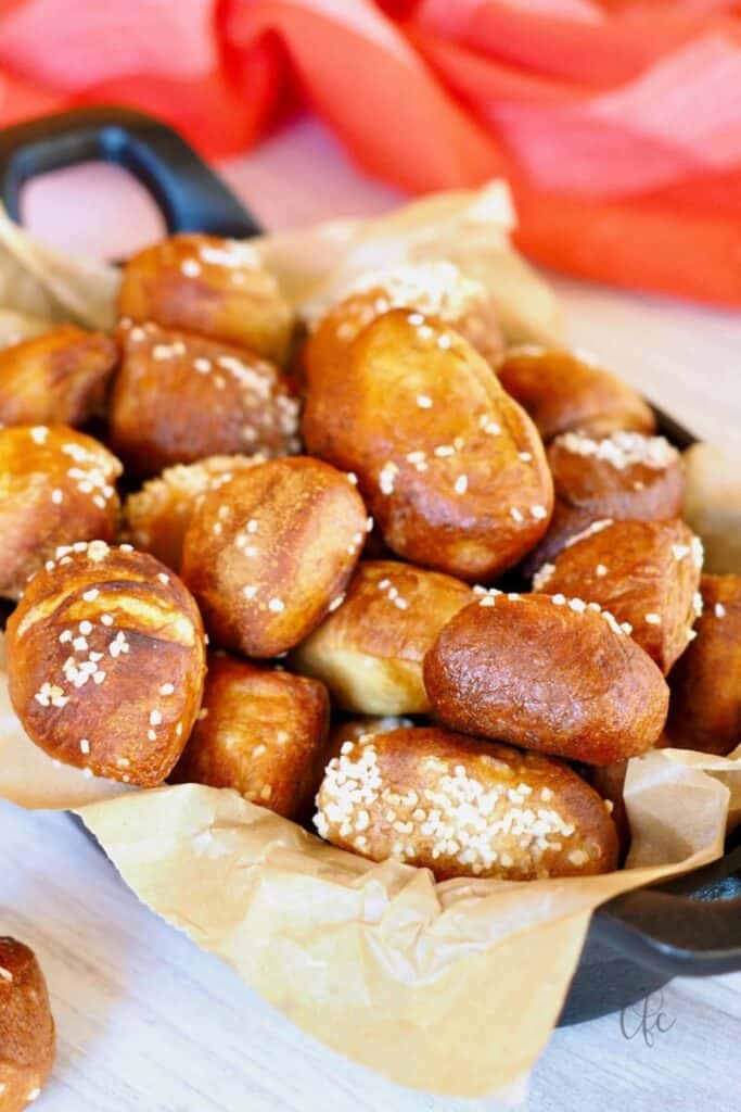 A skillet lined with parchment paper filled with easy pretzel bites baked to a deep golden brown and topped with coarse salt. The soft bite sized pieces are piled together showing their chewy texture and lightly crisp exterior.
