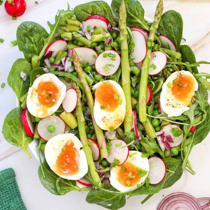 Overhead voew of plate of quick asparagus side salad topped with halved boiled eggs, beside a green tea towl, half a red onion and cut lemons.