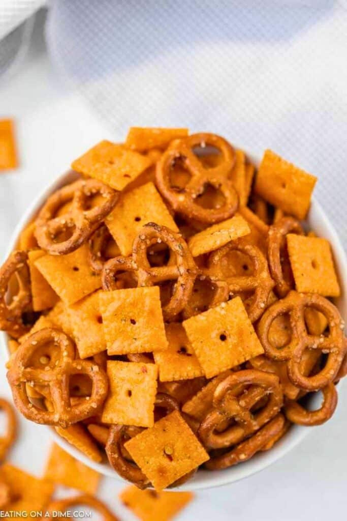 Bowl of spicy Cheez It snack mix made with Cheez It crackers and mini pretzels coated in a bold orange seasoning. The close up view highlights the crunchy texture and savory flavors, making this an easy snack for road trips, parties, or game day gatherings.