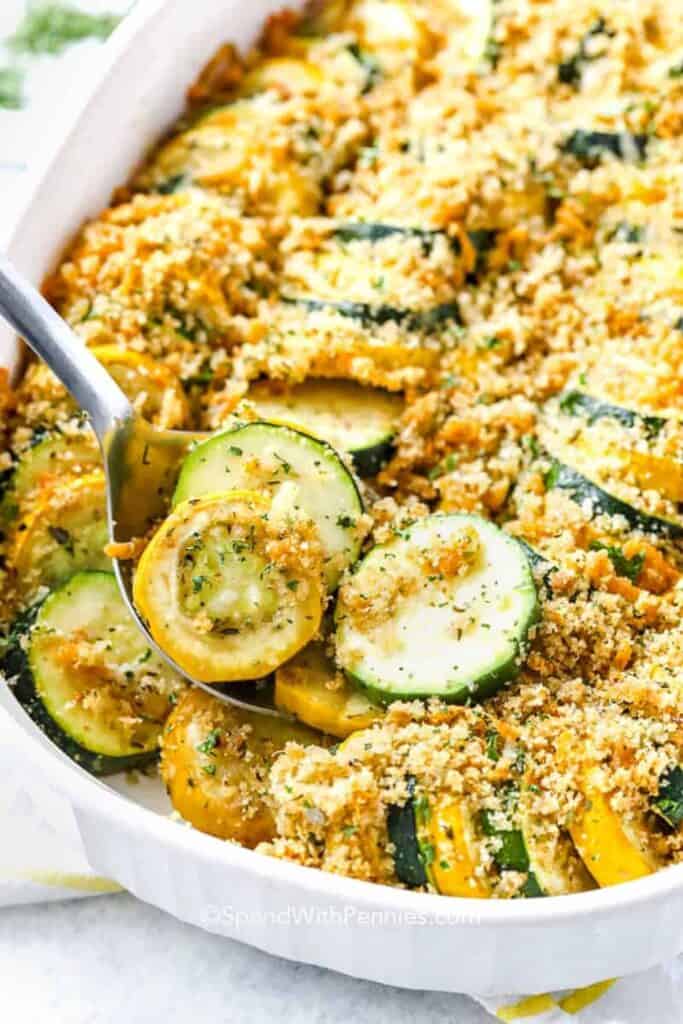 Vegetarian fall casserole with sliced zucchini and yellow squash topped with golden breadcrumbs, Parmesan cheese and herbs in a white oval baking dish.
