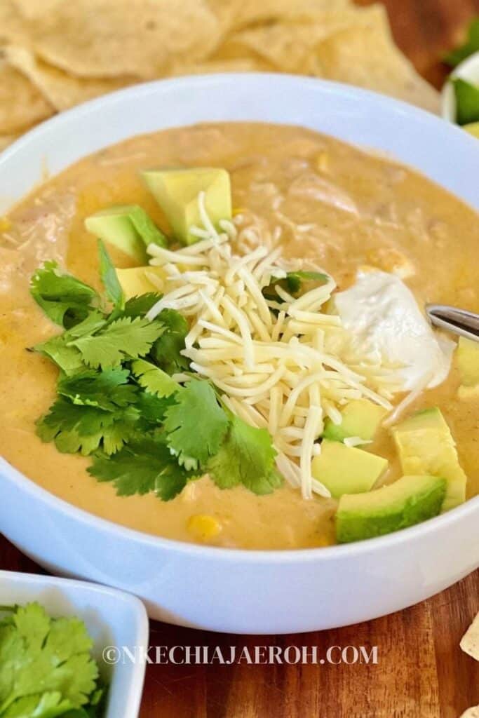 Bowl of white chicken chili topped with cilantro, avocado & cream cheese