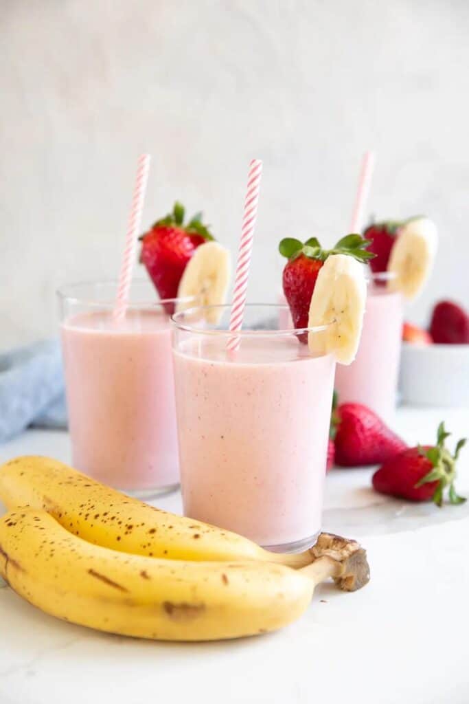 Three glasses of strawberry banana smoothie with striped pink & white straws. 