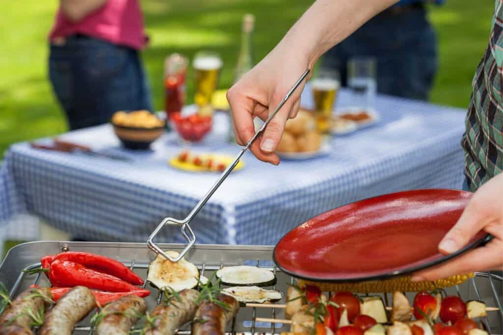 Woman working the grill, with two peopl in background by an outdoor table.