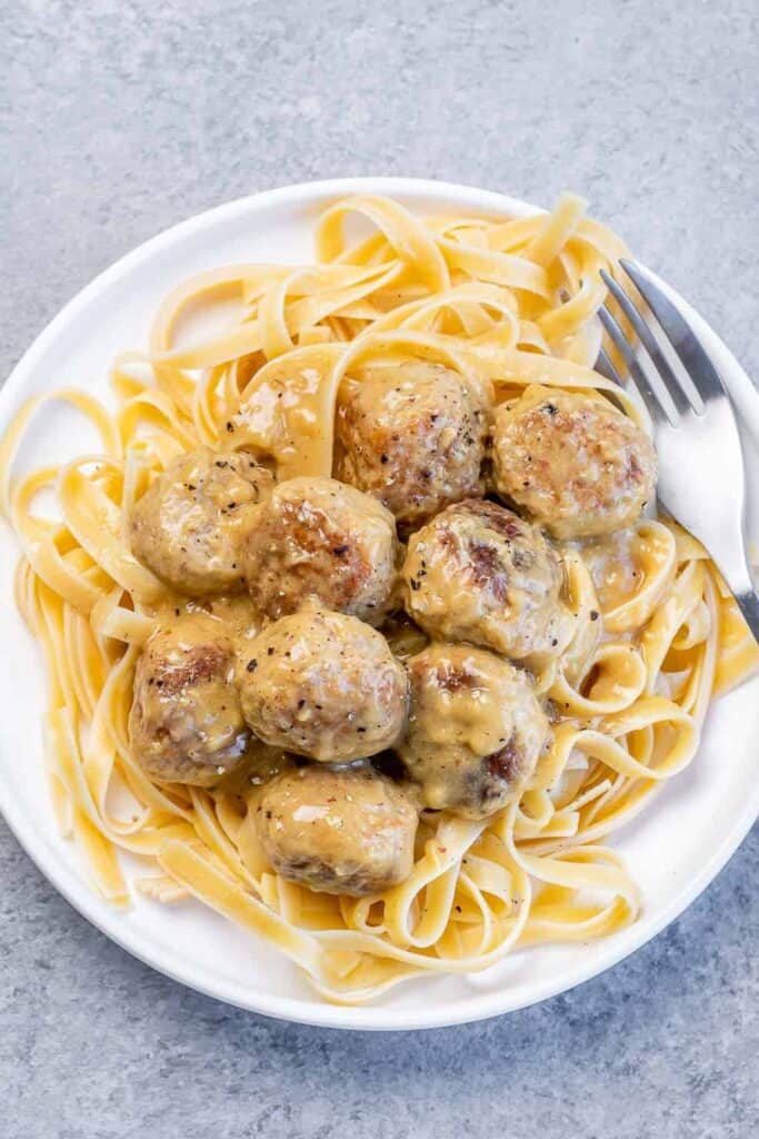 Plate of linguine noodles topped with swedish meatballs. 