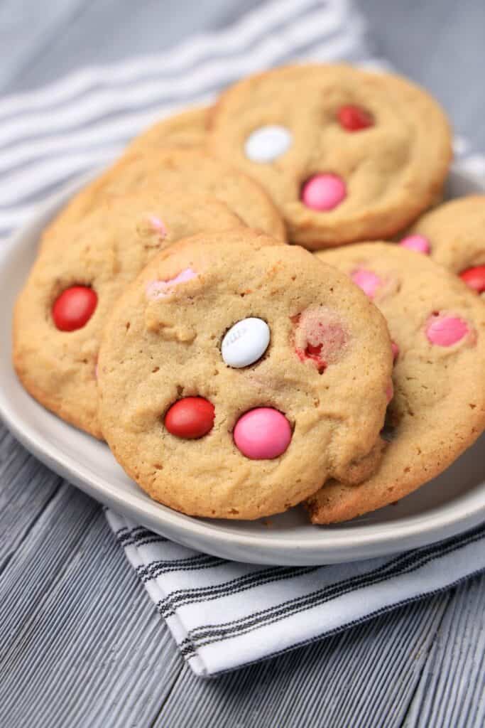 Plate of 6 peanut butter, M&Ms Valentine's Day cookies on a wooden background.