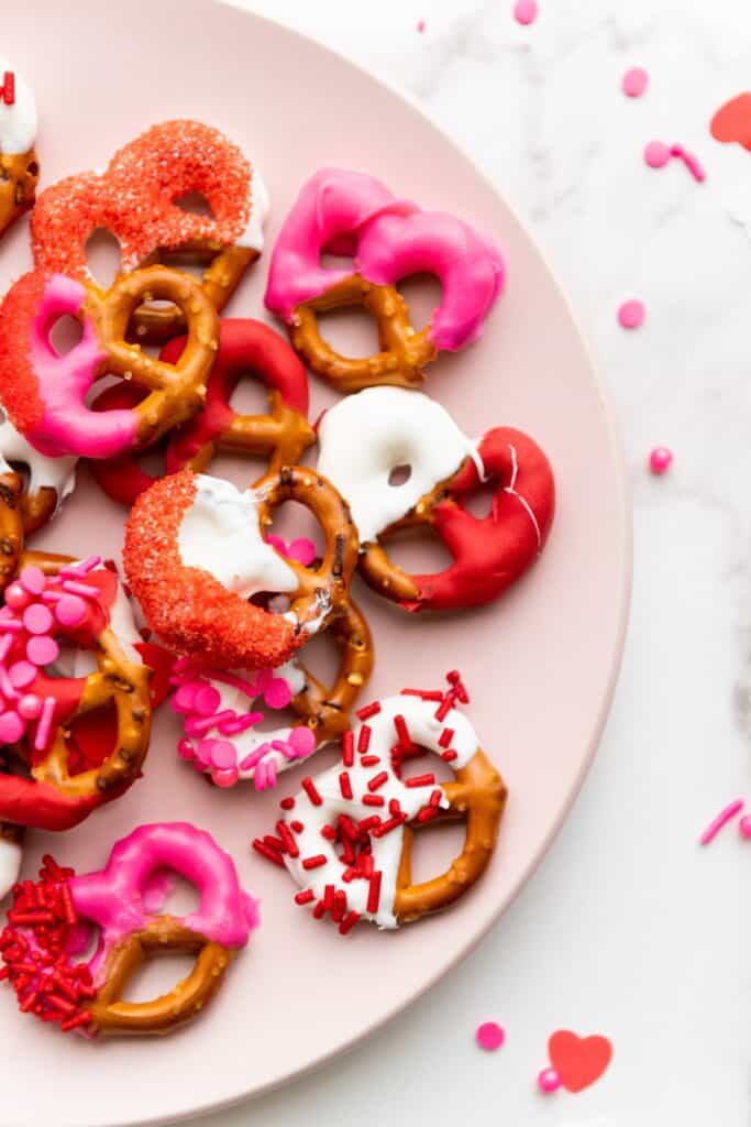 Half a plate of Valentine's Day pretzels dipped in red, white and pink candy melts and sprinkles for decoration.