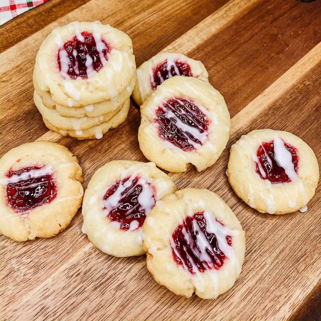 Two rows of raspberry jam thumbprint cookies on wooden board. 