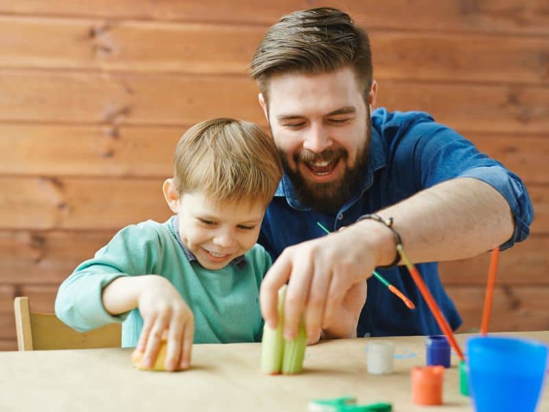 Father and son using apples as stamps to make art.