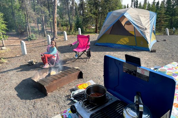 Young girl smiling in front of campfire and camp stove with chili & tea pot