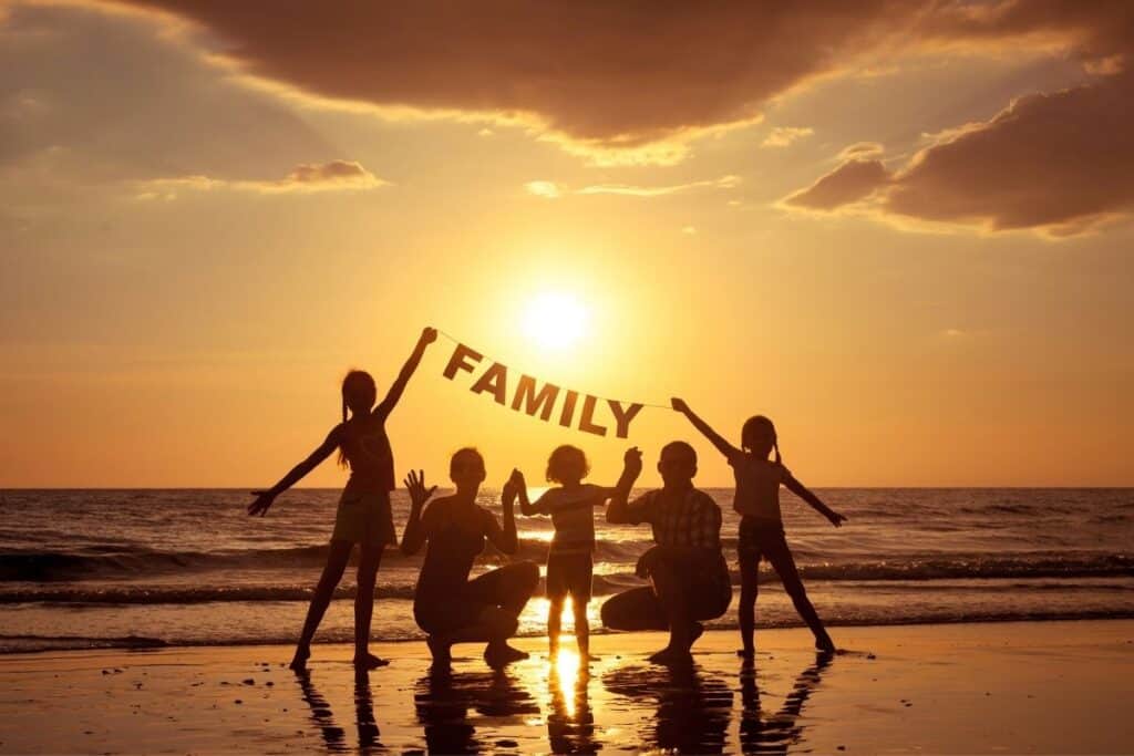 Silhouette of family of five at sunset on the beach, holding a sign that reads family.