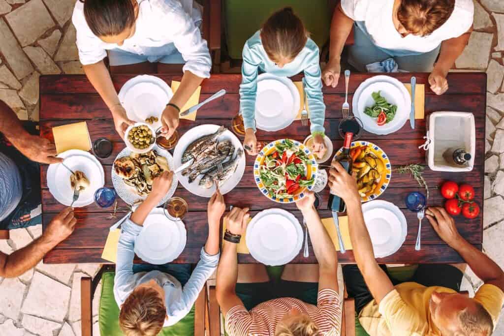 Overhead shot of large family eating a vacation dinner on a wooden table.