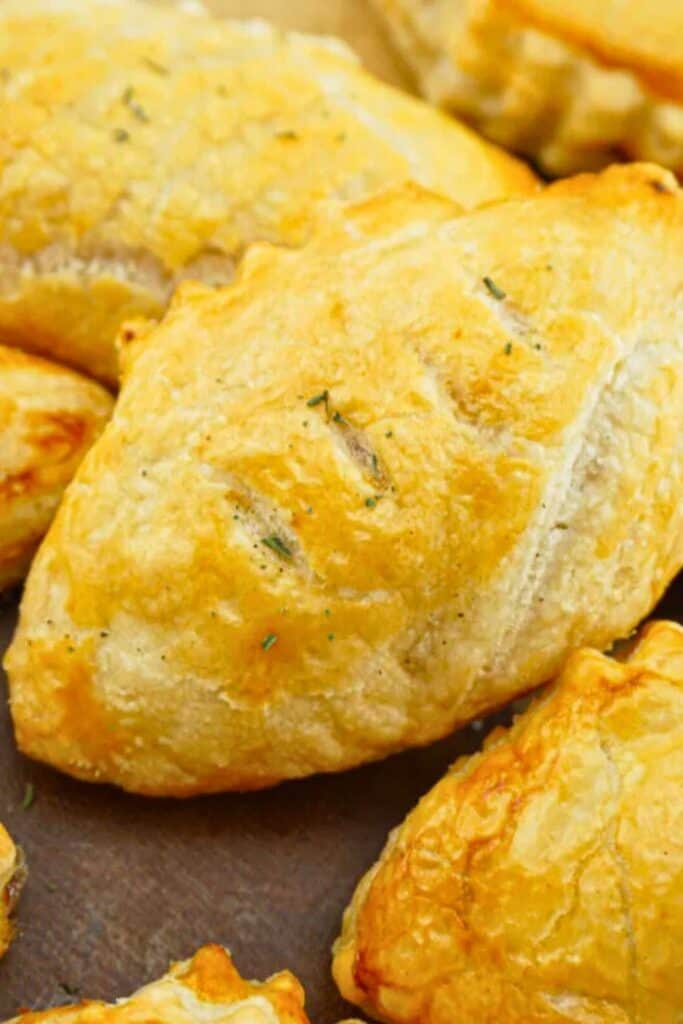 Golden-brown football-shaped puff pastries with a flaky, buttery crust, lightly brushed and baked to perfection, ideal for serving as a fun and savory snack at sports-themed gatherings.