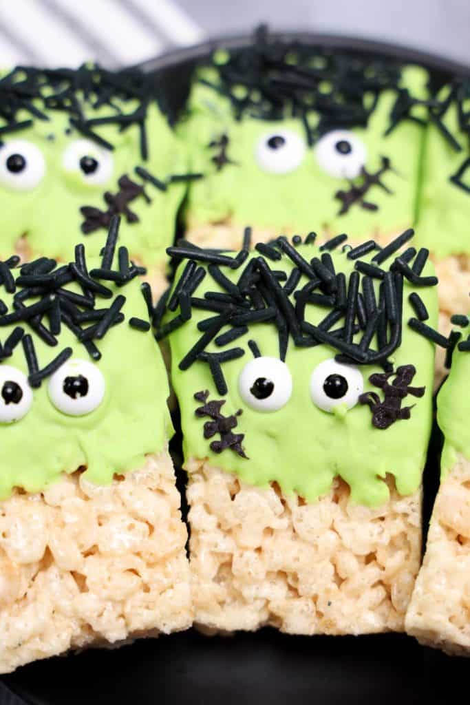 Rice Krispies treats decorated as Frankenstein faces with green candy coating, candy eyes, black sprinkle hair, and stitched mouth details.