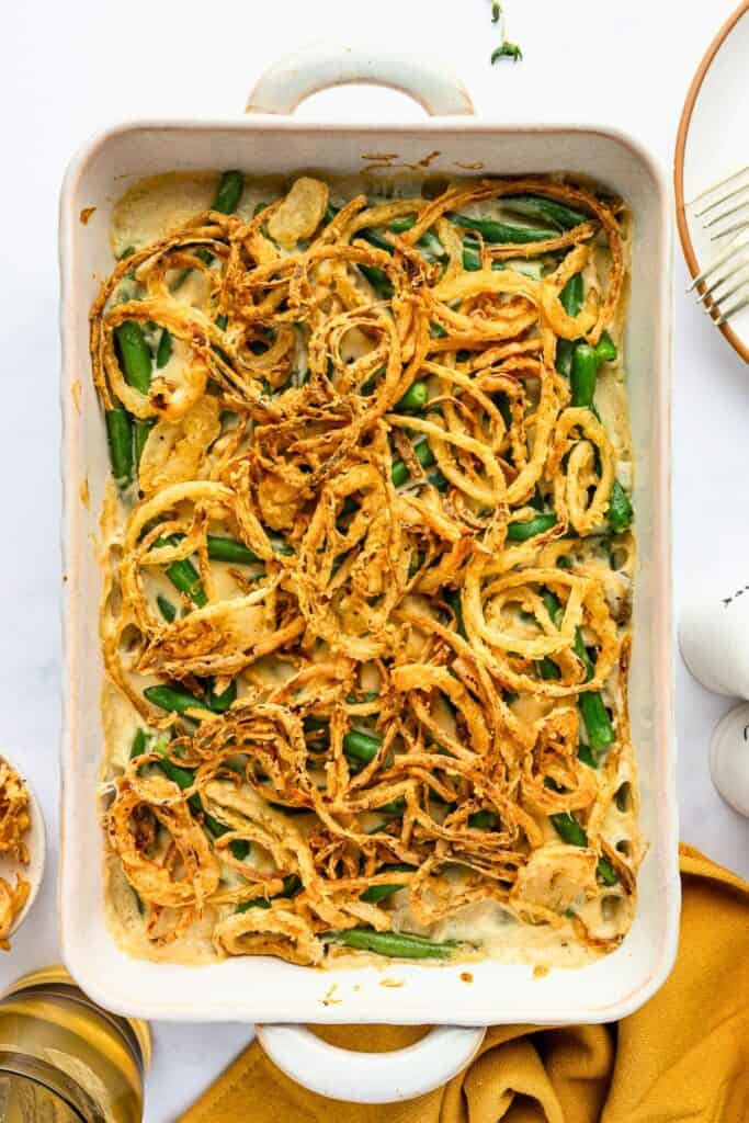 Fresh green bean casserole in a creamy mushroom sauce topped with crispy golden fried onions in a rectangular baking dish.
