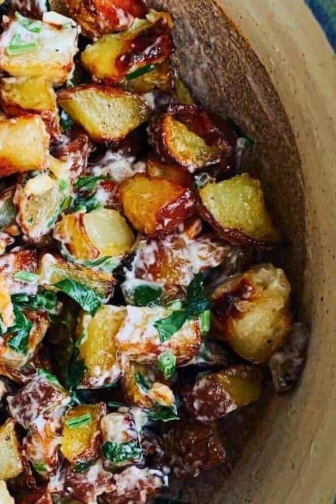 Garlic roasted potato salad made with crispy golden roasted potatoes tossed in a creamy dressing and sprinkled with fresh chopped herbs. The potatoes have caramelized edges and are mixed with green onions and parsley for a warm, savory side dish.