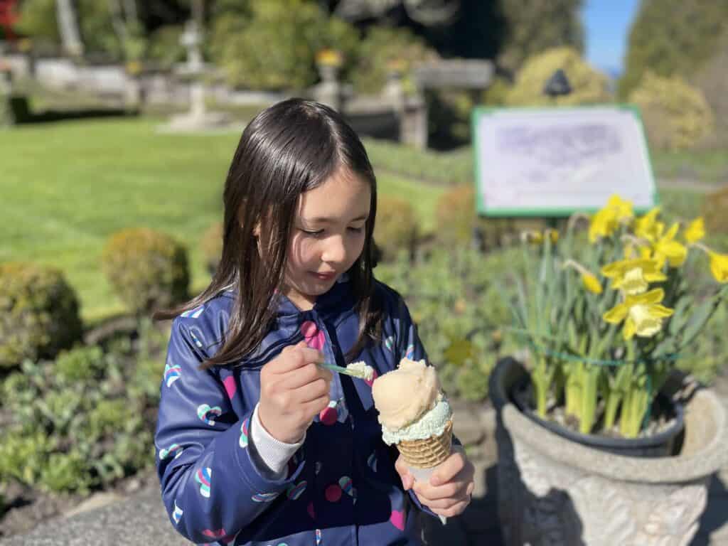 Young girl eating gelato in a cone in front of daffodils at Butchart Gardens Canada. 