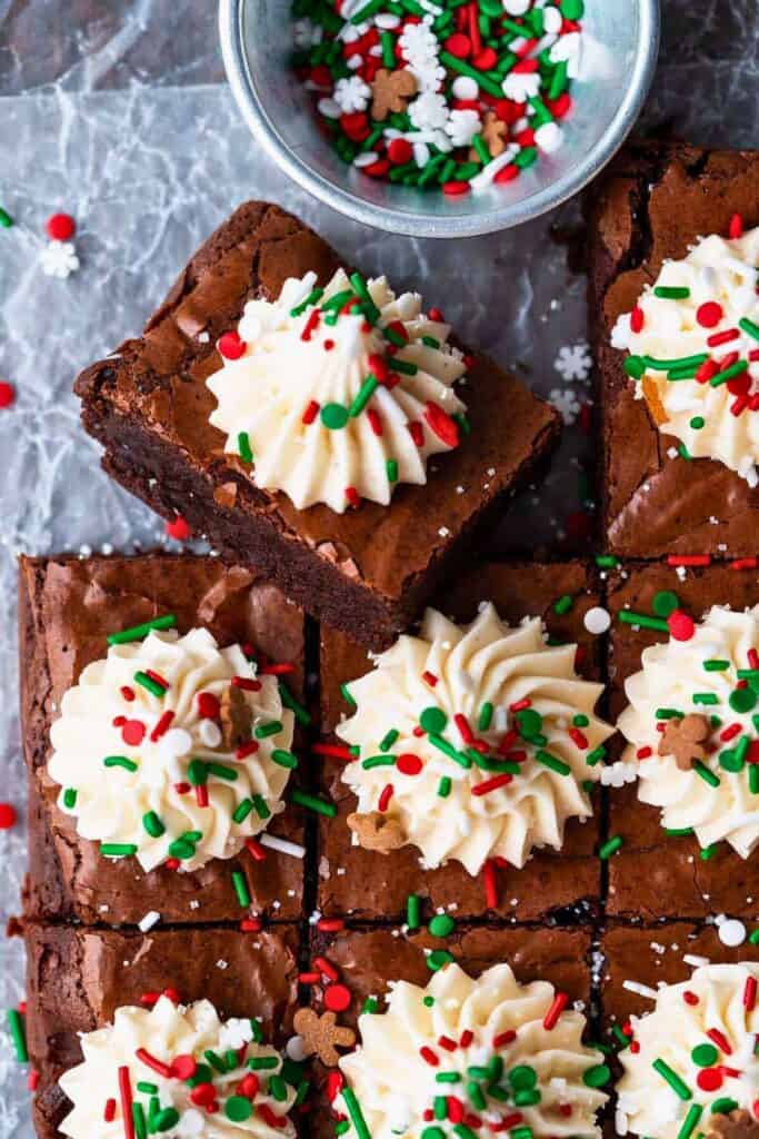 Fudgy gingerbread Christmas brownies topped with piped eggnog frosting and festive red, green, and white sprinkles, including mini gingerbread men and snowflakes.