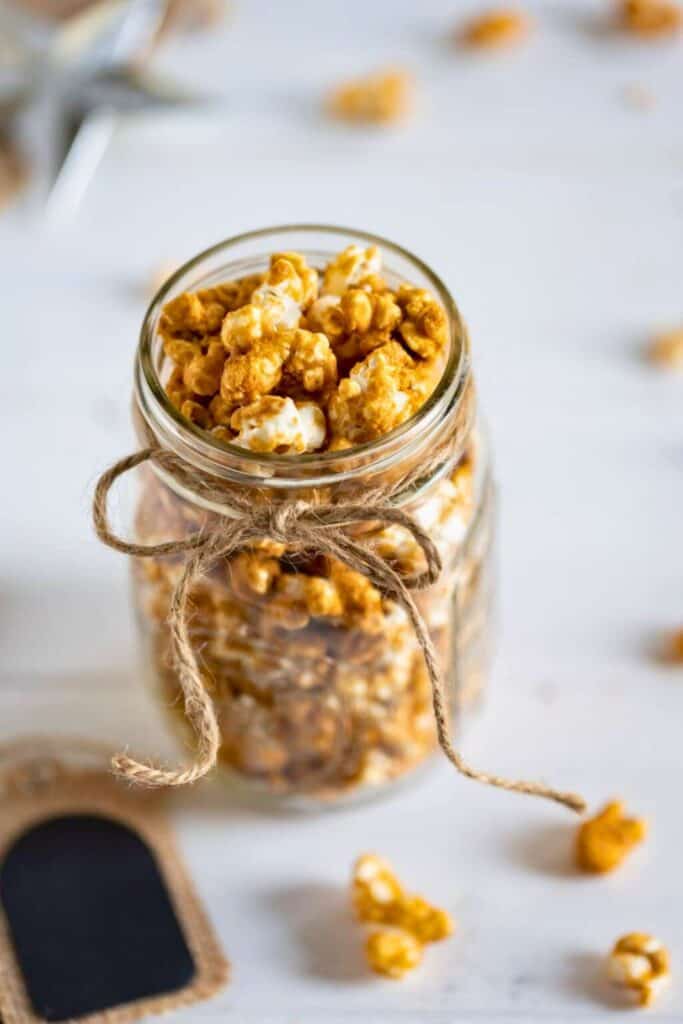 A mason jar filled with golden caramel popcorn tied with rustic twine, offering a sweet and crunchy treat that’s perfect as a movie night snack for adults and kids alike.