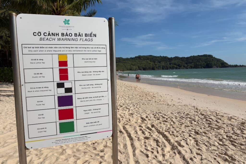 Sign explaining what the beach warning flags mean, with white sandy beach on a sunny day in the background. 