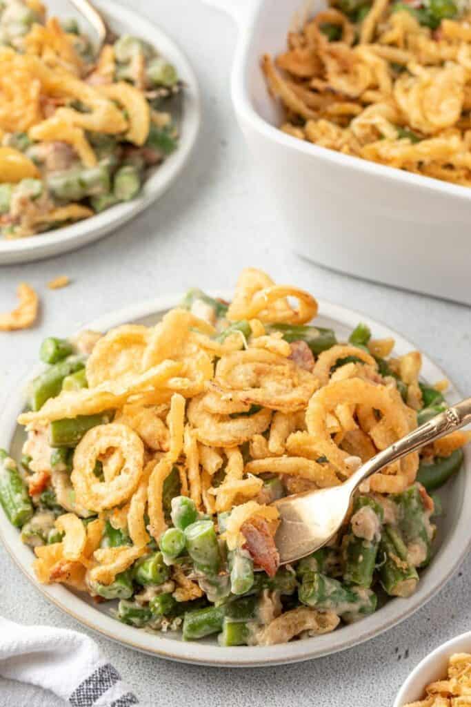 A serving of creamy green bean casserole side dish made with tender green beans and pieces of bacon in a rich sauce, topped generously with crispy fried onions.
