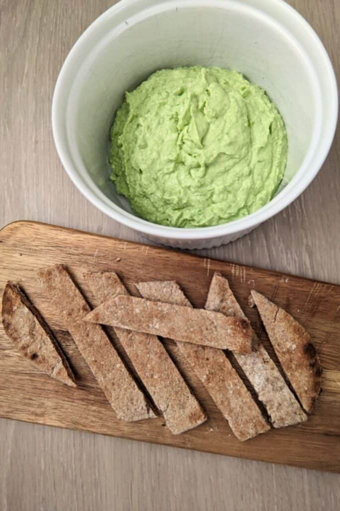 Close up of a dish of feta and green pea dip with pita strips. 