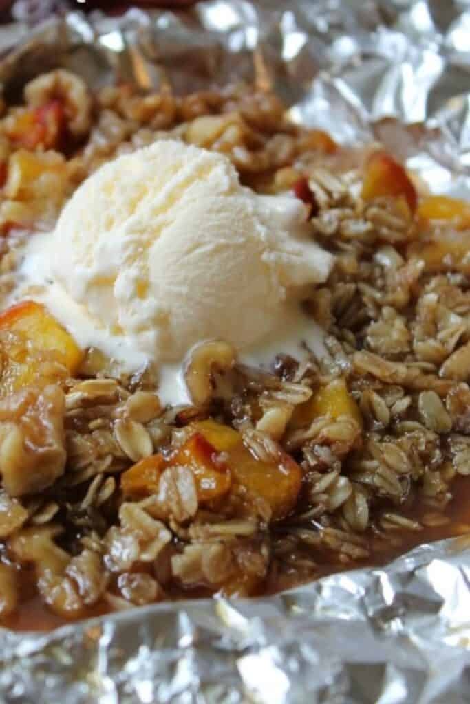 Peach crisp in a foil packet topped with a scopp of vanilla ice cream.