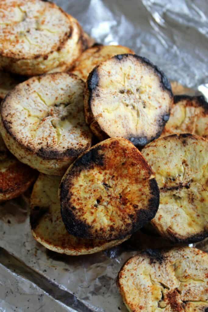 A linear pile of grilled plantain slices on a sheet of tin foil. 