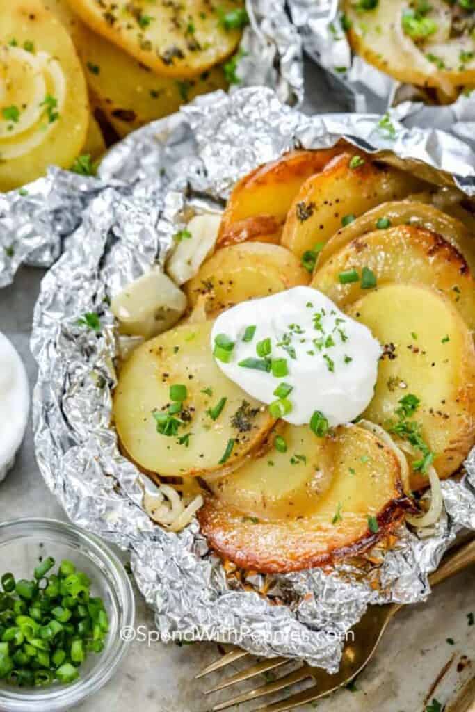 Foil packet open with grilled sliced potatoes inside topped with a dollop of sour cream and chives. 