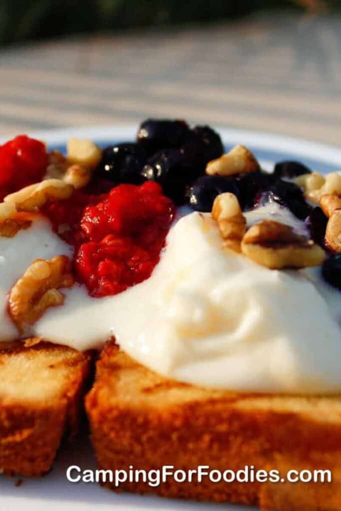 Two pieces of grilled pund cake, topped with mascarpone cheese, raspberries and blueberries.