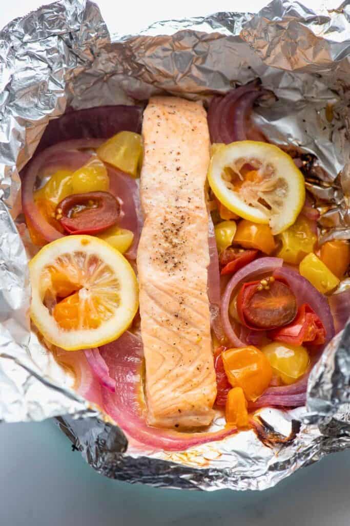 Overhead view of grilled salmon foil packet with slices of lemon, tomatoes, onions, yellow and orange peppers.