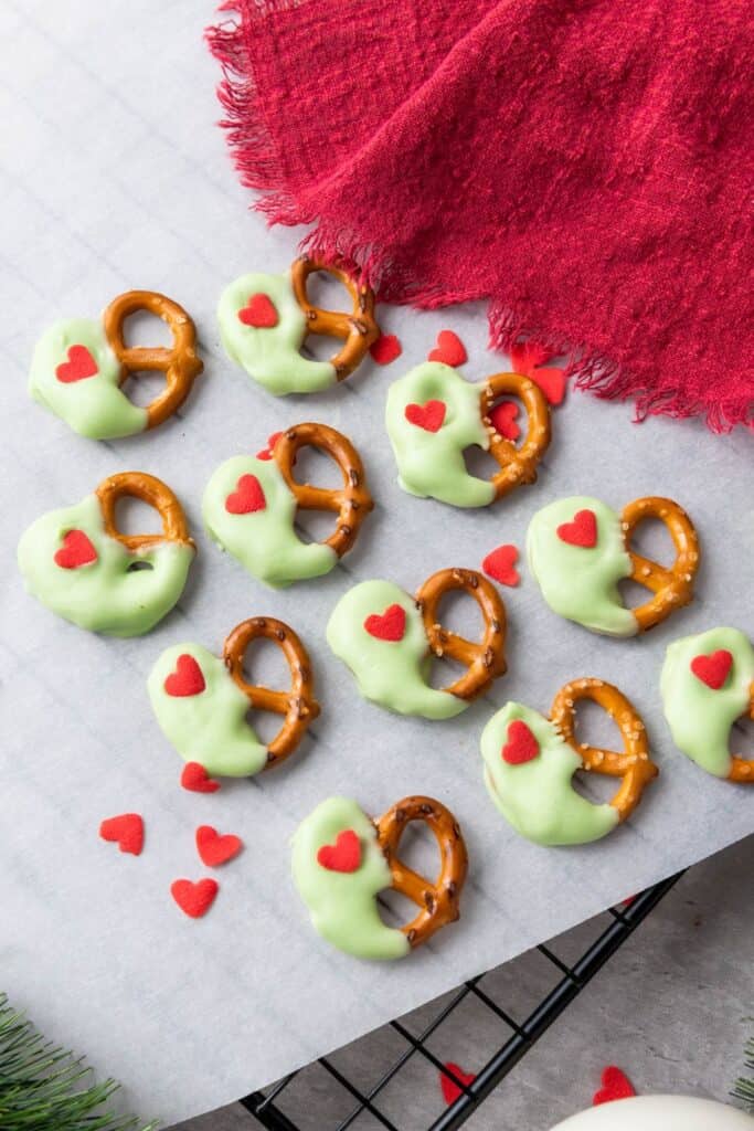 Close up of 11 grinch inspired pretzels, with half dipped in green candy melts and one small candy heart.