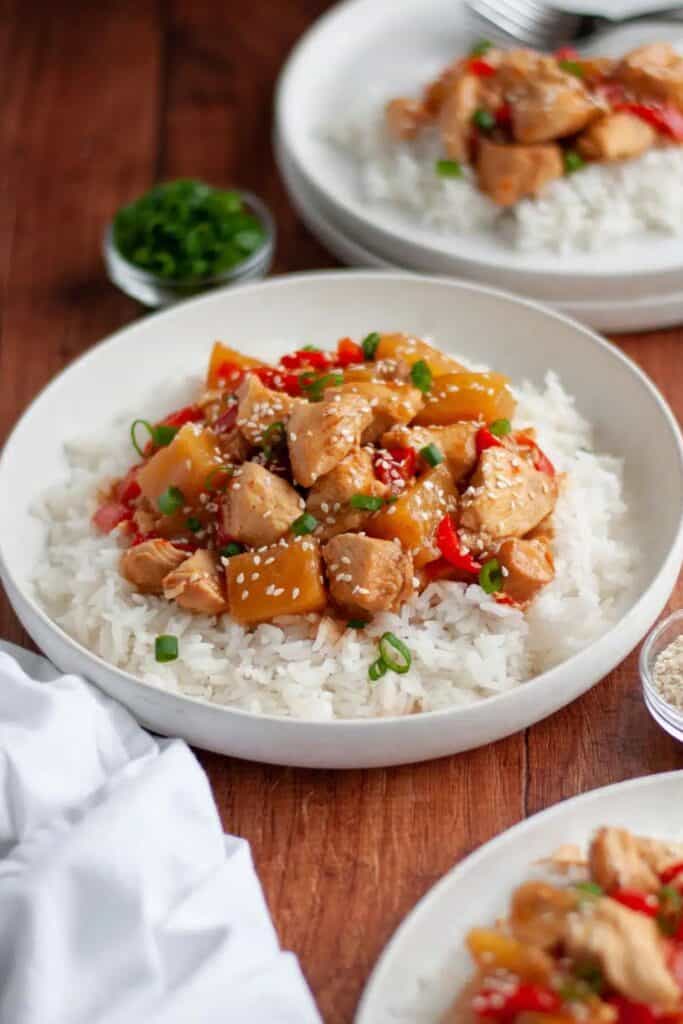 Two ceramic plates filled with white rice and topped with Hawaiian crockpot chicken & red peppers, sprinkled with sesame seeds and green onion slices. 